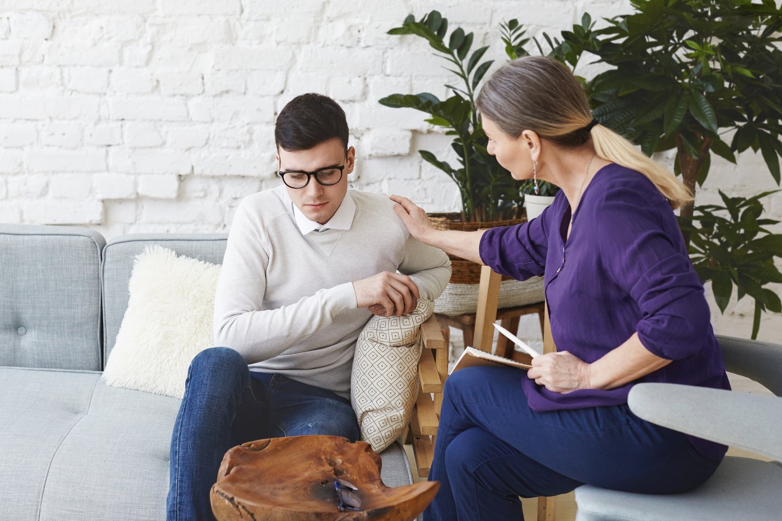 candid-shot-casually-dressed-professional-woman-psychotherapist-her-fifties-touching-her-young-male-patient-by-shoulder-while-having-counseling-session-expressing-sympathy-support